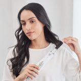 A woman with long, dark, wavy hair using a hair styler to curl a section of her hair