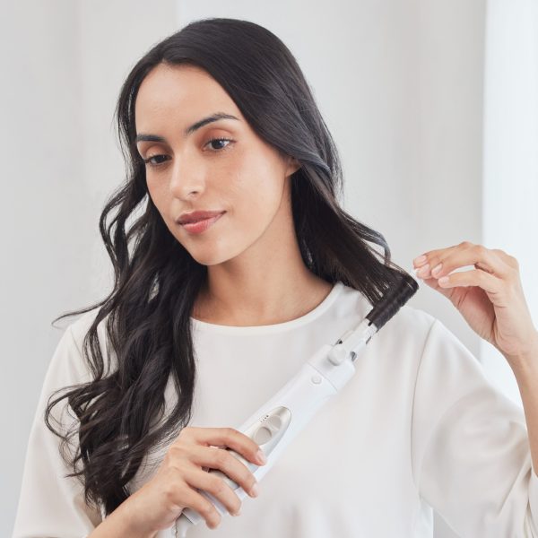 A woman with long, dark, wavy hair using a hair styler to curl a section of her hair